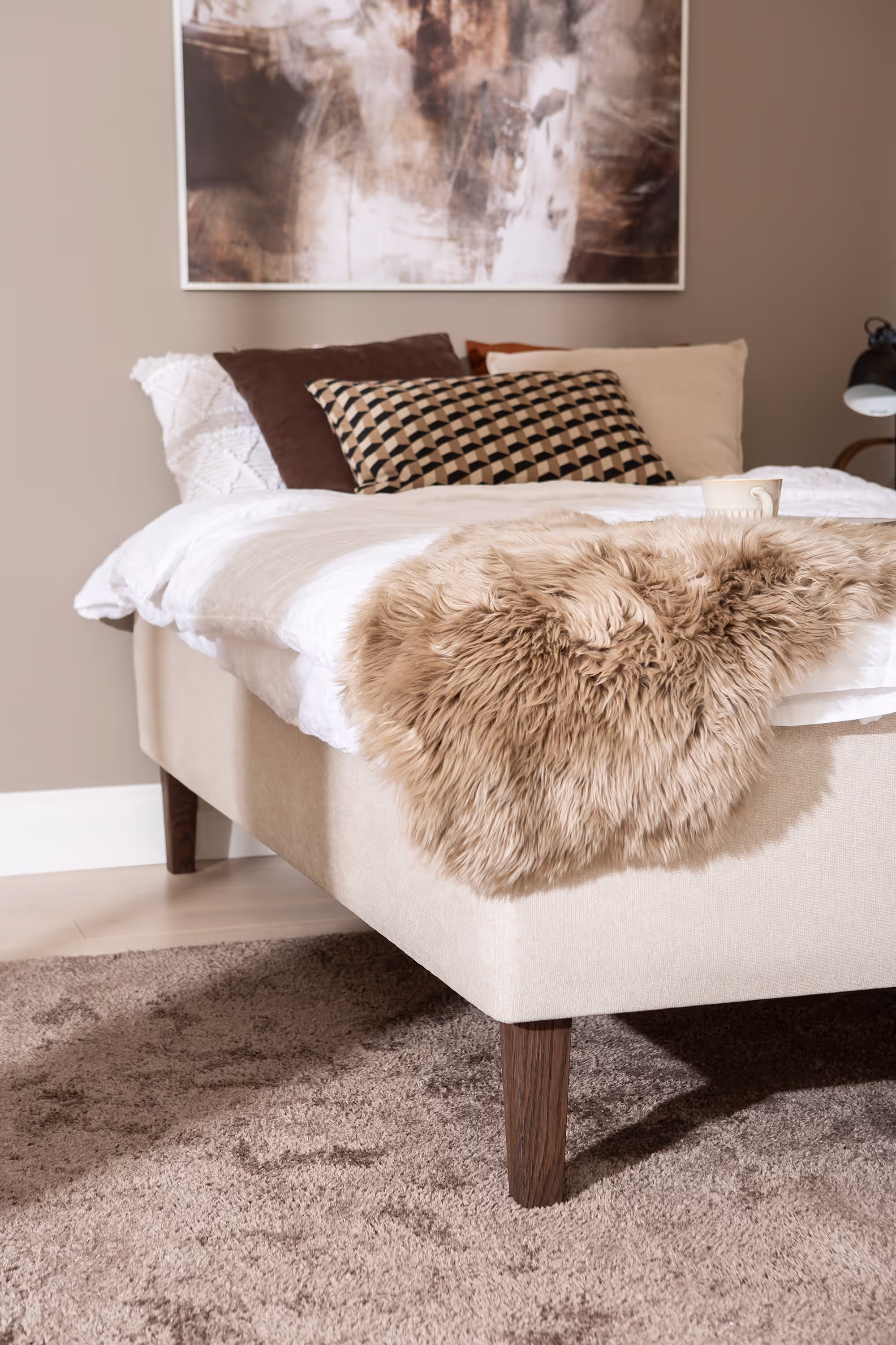 Side perspective of the Moon Gold divan bed 120x200 cm emphasizing the sturdy oak-stained wooden legs and beige fabric finish.